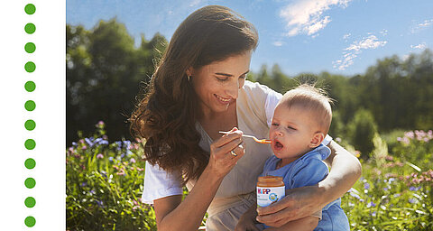 A woman is feeding a baby in a field.