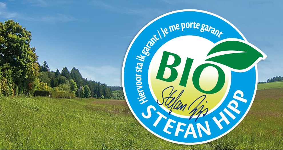 Un paysage avec des arbres et de l'herbe est recouvert d'un logo circulaire bleu avec le mot "BIO" et le nom "Stefan Hipp".