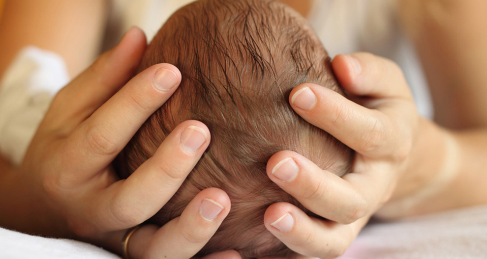 Een close-up van iemands handen die zachtjes het hoofd van een baby wiegen.