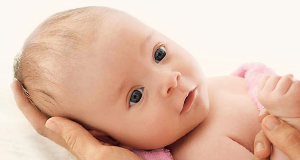 Een close-up van het gezicht van een baby, met een hand die zachtjes het hoofdje wiegt, tegen een zachte, neutrale achtergrond.