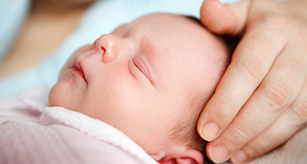 Een close-up van het gezicht van een pasgeboren baby, gedeeltelijk gewiegd door een hand.