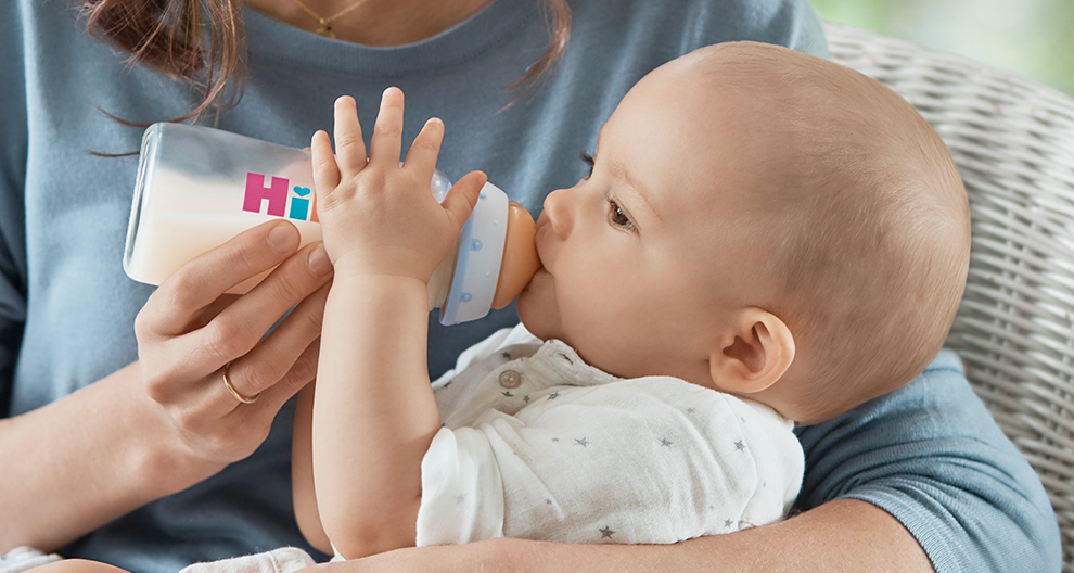 Een vrouw in een blauw shirt voedt een baby met een fles.