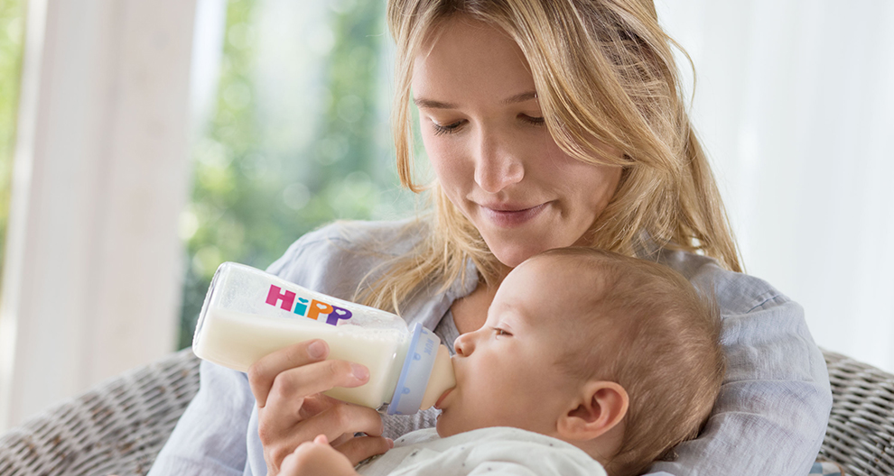 Een vrouw voedt een baby met een Hipp fles.