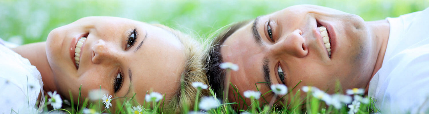 Two individuals lie face to face on grass with white flowers.
