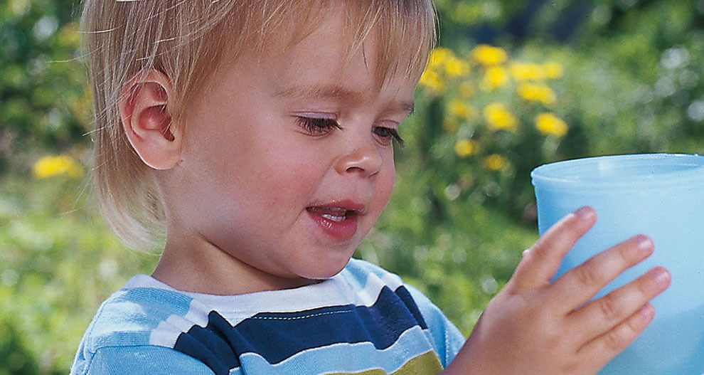 A young child is holding a blue cup outdoors.