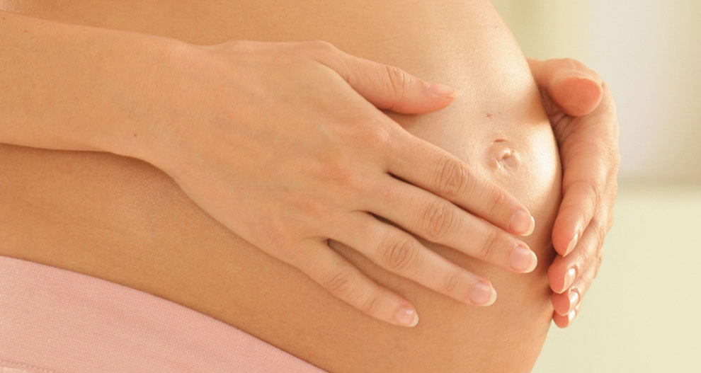 A pregnant woman's hands gently rest on her belly.